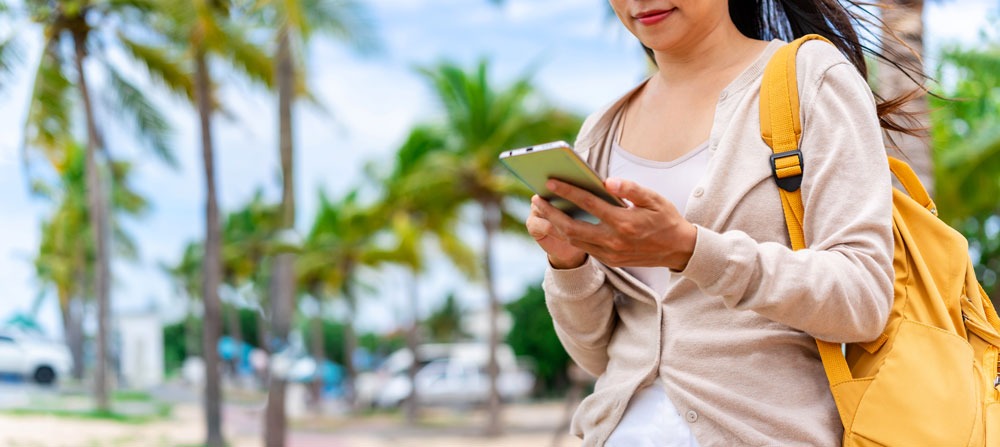 Woman using smartphone outdoors in a tropical setting, surrounded by palm trees, representing digital engagement for local businesses in Cairns.