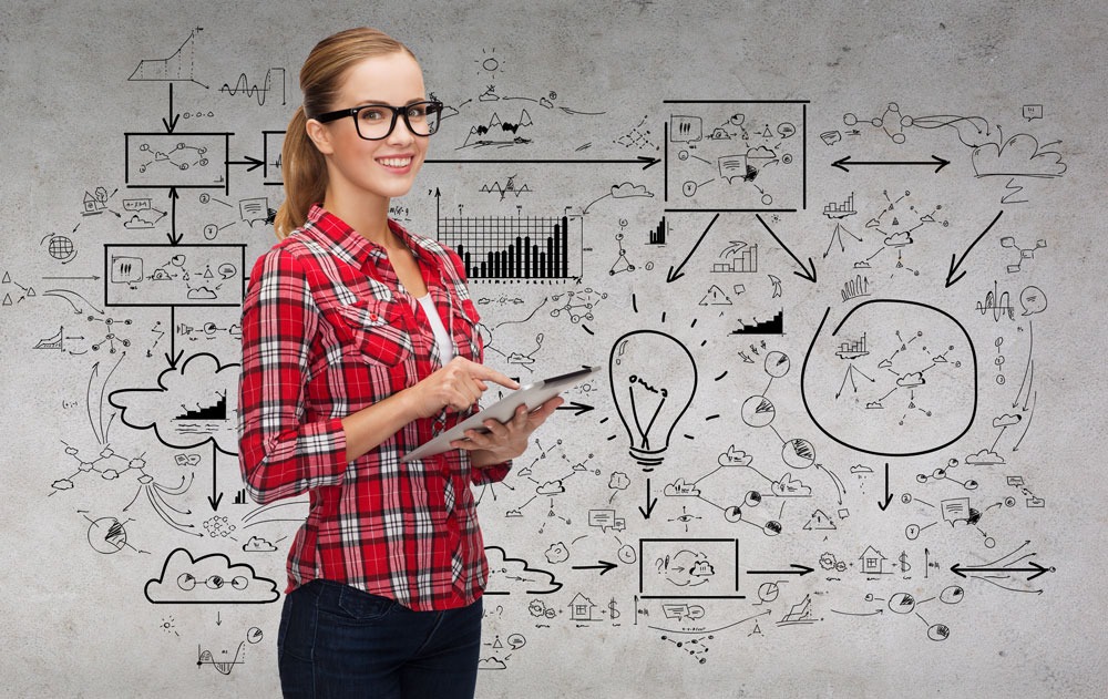 Smiling woman with glasses holding a tablet, standing in front of a wall covered with business diagrams and graphs, representing digital marketing and SEO strategies for Perth businesses.